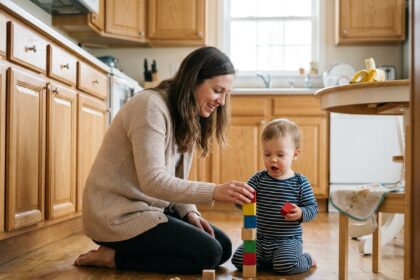 Jeune femme accroupie sur un plancher en bois jouant avec un tout-petit qui empile des cubes colorés dans une cuisine domestique chaleureuse